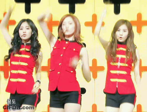 Three Girls Are Dancing In Front Of A Yellow Wall With Chinese Writing GIF