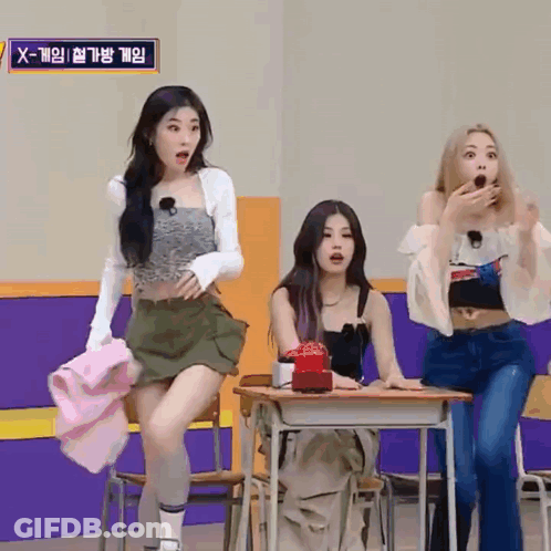 Three Girls Are Sitting At Desks In A Room With A Sign That Says X-Game On It . GIF