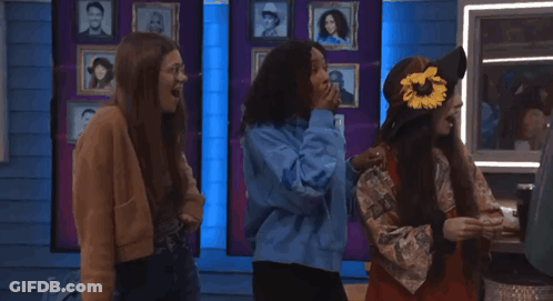 Three Girls Are Standing In Front Of A Wall With Pictures Of People GIF