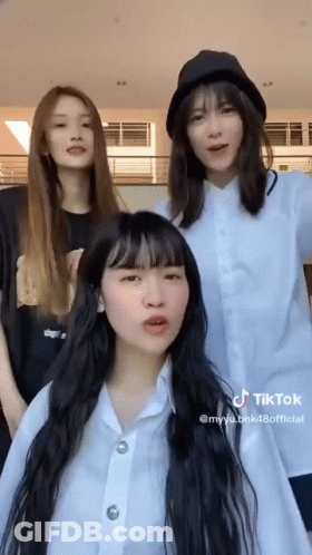 Three Girls Are Standing Next To Each Other In A Room . One Of The Girls Is Wearing A Hat . GIF