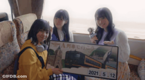 Three Girls Sitting On A Bus Holding A Sign That Says 2021.05.12 GIF