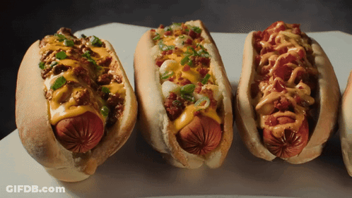 Three Hot Dogs With Different Toppings On Them GIF