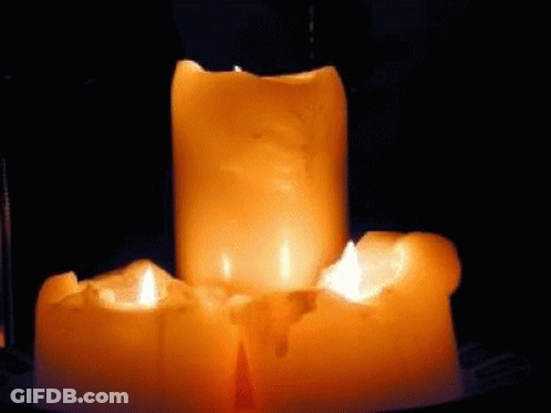 Three Lit Candles Are Sitting On Top Of Each Other On A Table In The Dark . GIF