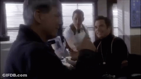 Three Men Are Sitting At A Table In A Room Talking To Each Other . GIF