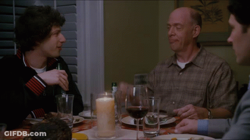 Three Men Are Sitting At A Table With A Candle And Wine GIF