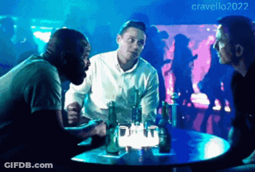 Three Men Are Sitting At A Table With Bottles Of Beer In Front Of A Crowd With The Year 2022 On The Bottom GIF