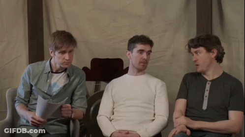 Three Men Are Sitting In Chairs And One Of Them Is Reading A Piece Of Paper GIF
