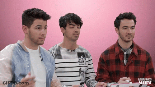Three Men Are Sitting In Front Of A Pink Background That Says Popbuzz Meets On It GIF