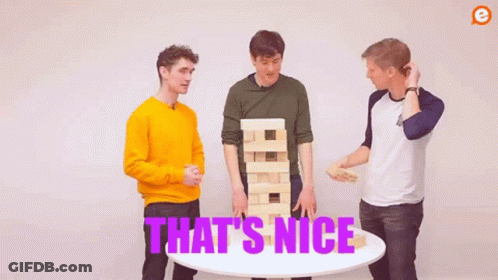 Three Men Are Standing Around A Table With A Jenga Tower . GIF