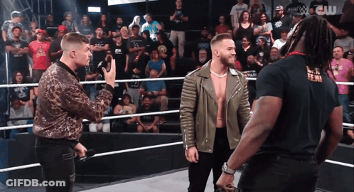 Three Men Are Standing In A Wrestling Ring And One Of Them Is Wearing A Black T-Shirt That Says W.c. GIF