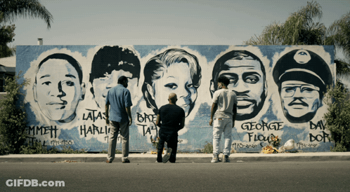 Three Men Are Standing In Front Of A Mural Of George Floyd 'S Face GIF