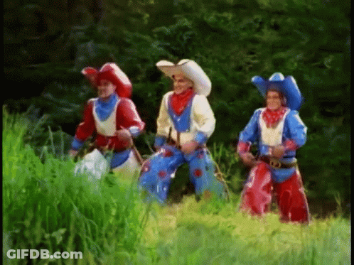 Three Men Dressed In Cowboy Costumes Are Standing In A Grassy Field GIF