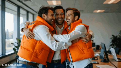 Three Men In Orange Vests Hugging Each Other In An Office GIF
