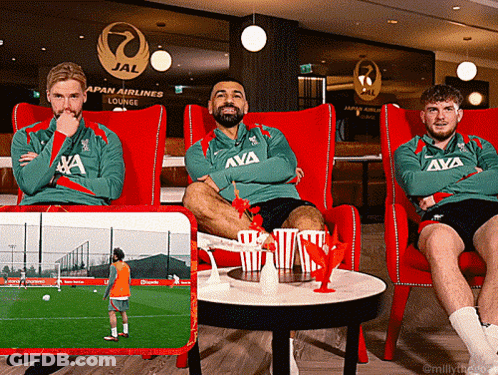 Three Men Sit In Red Chairs In Front Of A Japan Airlines Lounge Sign GIF