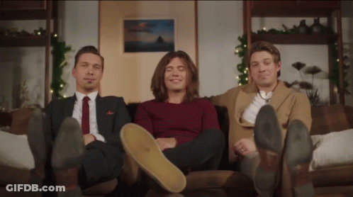 Three Men Sitting On A Couch With Their Feet On The Floor GIF