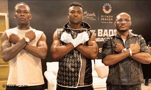 Three Men Standing In Front Of A Sign That Says Saudi Season GIF