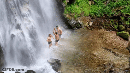 Three Men Swimming Under Waterfall Hands In Air GIF