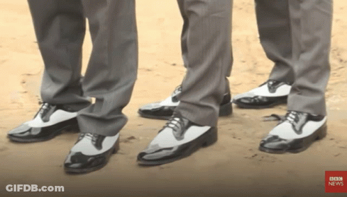 Three Men Wearing Suits And Black And White Shoes Are Standing Next To Each Other With Bbc News In The Corner GIF