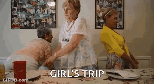 Three Older Women Are Standing Around A Table With The Words `` Girl 'S Trip '' Above Them . GIF
