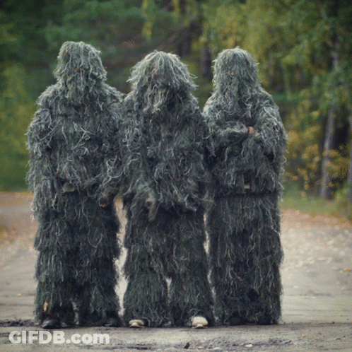 Three People Are Standing On A Dirt Road Wearing Sniper Suits GIF