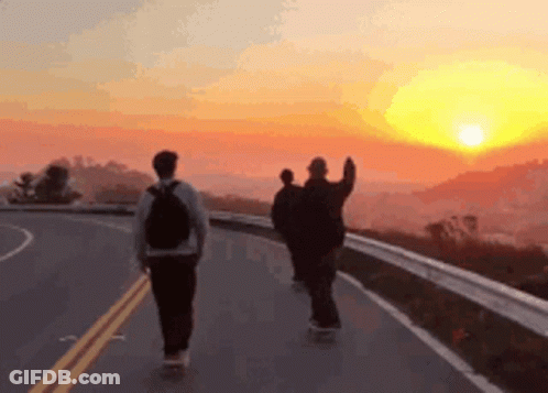 Three People Are Walking Down A Road At Sunset GIF