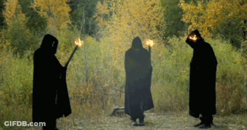 Three People In Black Cloaks Holding Torches GIF