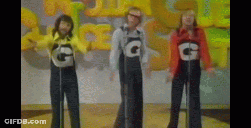 Three People Wearing Overalls With The Letter G On Them Singing Into Microphones GIF