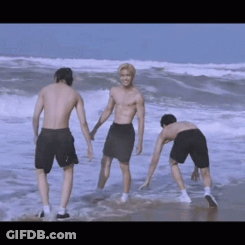 Three Shirtless Men Are Standing On The Beach Holding Hands GIF