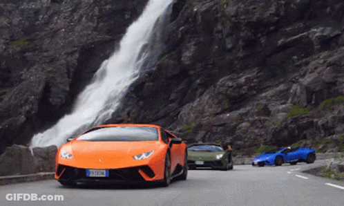 Three Sports Cars Are Driving Down A Road Near A Waterfall GIF