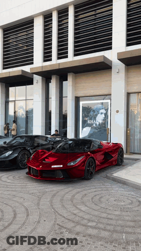 Three Sports Cars Parked In Front Of Khan Sign GIF