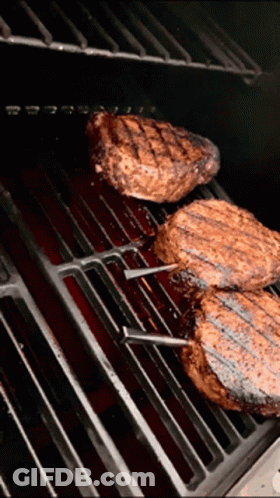 Three Steaks Are Cooking On A Grill With A Red Sauce GIF