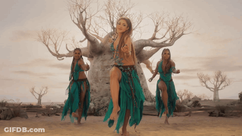 Three Women Are Dancing In Front Of A Tree In A Desert GIF