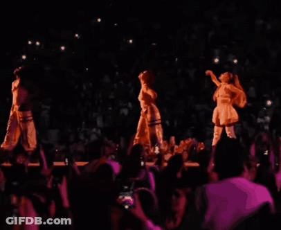 Three Women Are Dancing On A Stage In Front Of A Crowd In A Dark Room . GIF