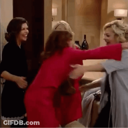 Three Women Are Hugging Each Other In A Room . One Of The Women Is Wearing A Red Dress . GIF