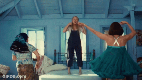 Three Women Are Jumping On A Bed With One Wearing A Green Dress GIF