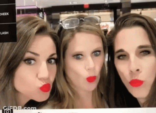 Three Women Are Making Funny Faces In Front Of A Sign That Says Cheek Lash And Lipstick GIF