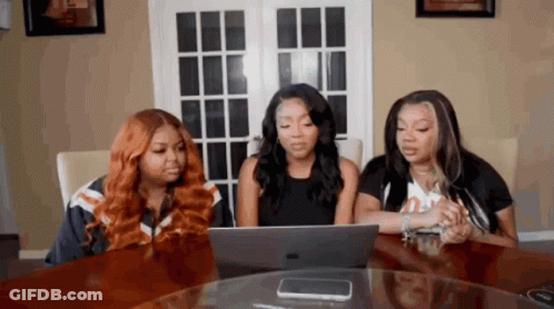 Three Women Are Sitting At A Table Looking At A Laptop Computer GIF