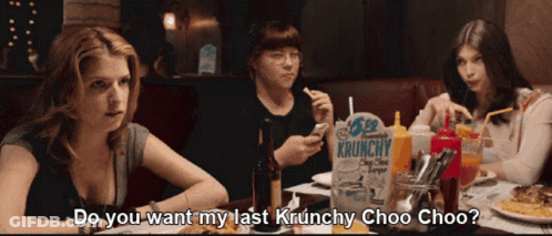 Three Women Are Sitting At A Table With A Box Of Krunchy Chips GIF