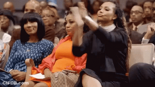 Three Women Are Sitting In A Crowd Of People And One Of Them Is Taking A Picture Of Herself With Her Phone . GIF