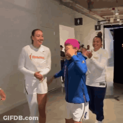 Three Women Are Standing In A Locker Room And One Of Them Is Wearing A White Shirt With The Word Basketball On It GIF