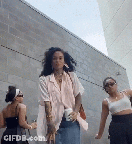 Three Women Are Standing In Front Of A Brick Wall And One Is Holding A Cup Of Coffee GIF