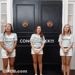 Three Women Are Standing In Front Of A Door With The Words `` Congrats Kk '' Written On It . GIF