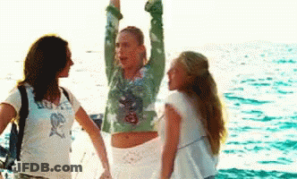 Three Women Are Standing On A Boat In The Ocean . One Of The Women Is Raising Her Arms In The Air . GIF