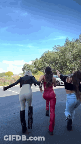 Three Women Are Walking Down A Street With Their Arms Outstretched . GIF