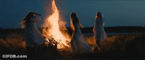 Three Women In White Robes Are Standing Around A Fire At Night . GIF