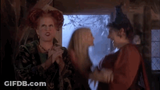 Three Women Standing With One In Witch Hat GIF