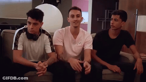Three Young Men Are Sitting On A Couch With One Wearing A Pink Shirt GIF