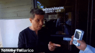 Tommy Tallarico Is Holding A Cell Phone In Front Of An Intelvision Secret Lair GIF