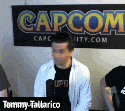 Tommy Tallarico Is Standing In Front Of A Large Capcom Sign GIF