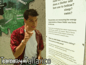 Tommy Tallarico Standing In Front Of Large Poster GIF